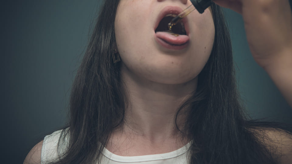 נערה צעירה מטפטפת שמן CBD על הלשון